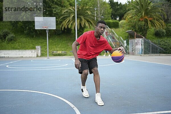 African american basketball player training in an outdoor urban court in the middle of a park