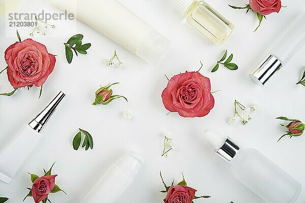 Flat lay cosmetic bottles and containers with pink roses and green leaves background on white table