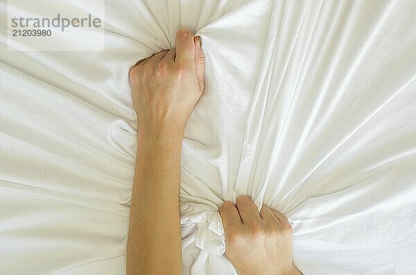 Hand sign orgasm of woman on white bed  Hand of female pulling white sheets in ecstasy  feeling and emotion concept