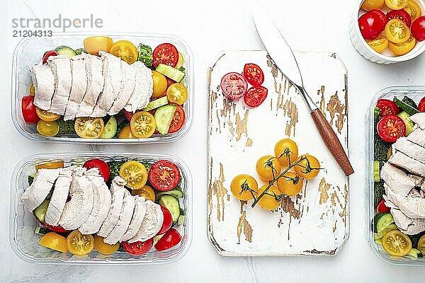 Healthy meal prep for lunch  diet boiled chicken fillet with vegetables salad in lunch boxes containers top view on white marble kitchen table background with knife and cutting board  food photography