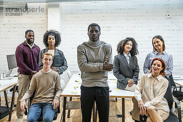 Porträt eines afrikanischen Mannes  der neben Coworking Kollegen steht  die um einen Tisch sitzen