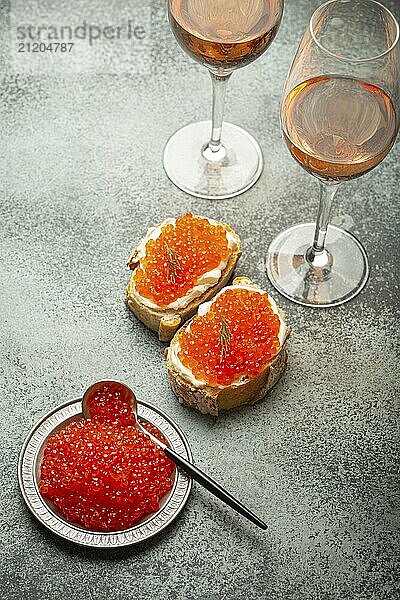 Kleiner Metallteller mit rotem Lachskaviar  zwei Kaviar Toasts Canape  zwei Gläser Champagner von oben auf grauem Betonhintergrund  festliche Luxusdelikatesse und Vorspeise  Foodfotografie