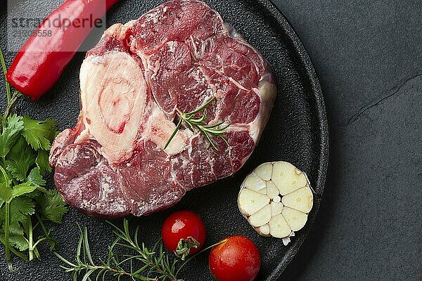 Food  Food  Raw fresh ossobuco con herbs  garlic and chile pepper on black plate. Dark background