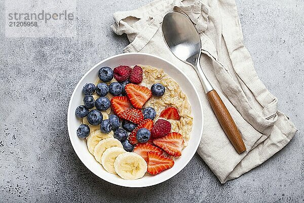 Haferflockenbrei mit Früchten und Beeren in Schüssel mit Löffel auf weißem hölzernen Hintergrund Tisch oben Ansicht  hausgemachte gesundes Frühstück Müsli mit Erdbeere  Banane  Heidelbeere  Himbeere  Lebensmittel Fotografie  food photography  food photography