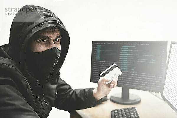 Cunning hacker fraudster in white background with stolen credit card in hand tries to steal money from bank account. Internet theft concept