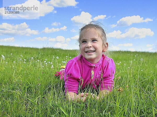 Happy smiling little girl lying on green grass