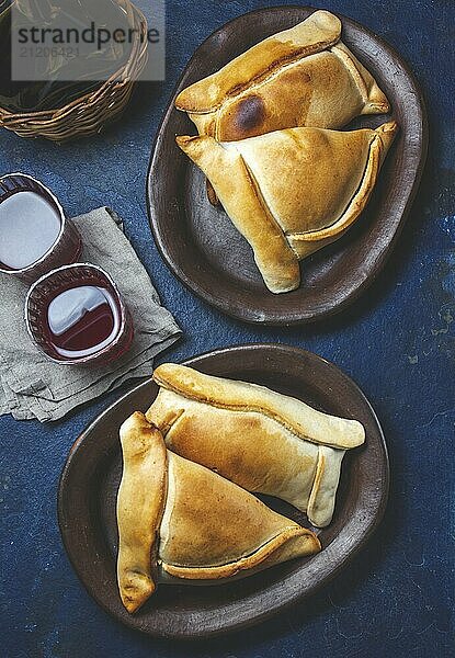 Food  Food  Tipical Chilean baked empanadas de pino y napolitano on clay plates with wine. Dish and drink on 18 September party Independence day Chile  blue background