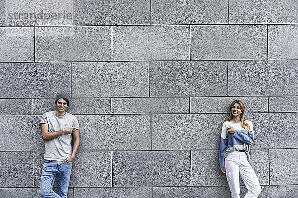 Cheerful couple at the street  show a big sale  or nice offer. Advertise concept. People  travel and tourism  on city street and couple show with their fingers something over gray wall background