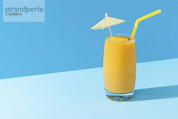 Glass of mango smoothie with summer decor on a blue background  in harsh light. Healthy smoothie drink. Vitamin breakfast beverage. Dietary mocktail