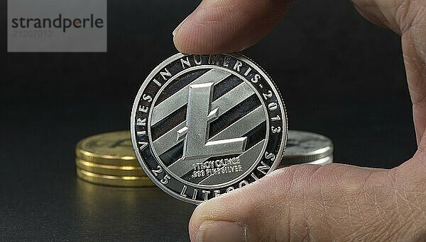 Hand showing litecoin with black background with a single litecoin facing the camera in sharp focus with shading on the icon letter B on the face of the bit coin