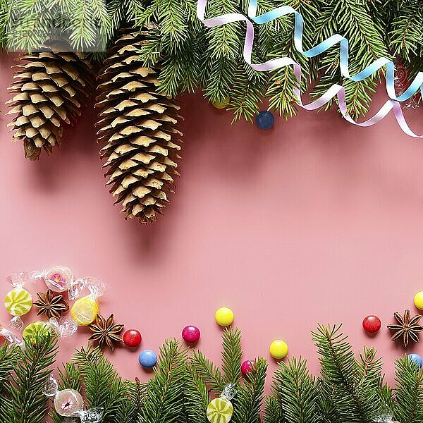 Flat lay design of Christmas greeting card of fir twigs cones  paper streamer  candies and spices on pink background. Space for text