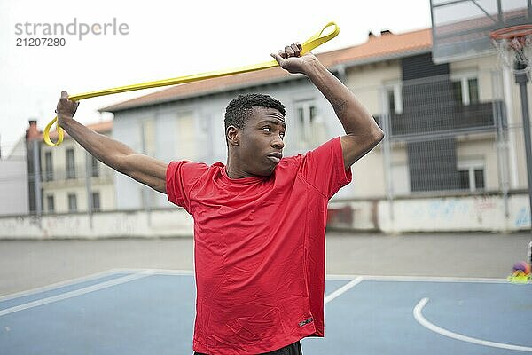 African teenager warming up using elastic band in an outdoor basketball urban court