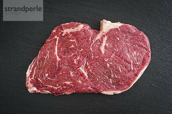 Fresh uncooked rib-eye steak on black background