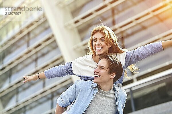 Man giving his pretty girlfriend a piggy back at street smiling at each other on a sunny day