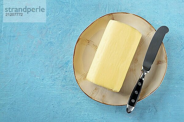 Eine Stange Butter mit einem Messer auf einem Teller  Top Shot auf blauem Hintergrund mit Platz für Text  Food Fotografie