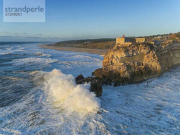 Aerial view of lighthouse on a cliff with a fortress on the coast of the Atlantic ocean with big waves at sunset in Nazare  Portugal  Europe