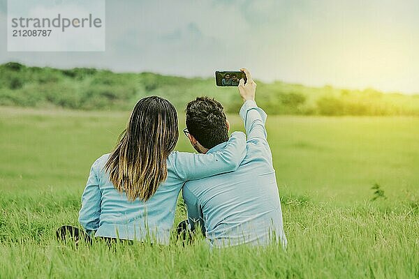 Couple in love taking a selfie sitting in a beautiful field. Young happy couple taking a selfie sitting in the field