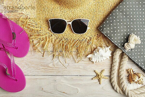 Straw hat sunglasses flip flops and beach bag on white wooden background