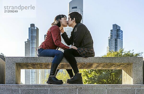 Charming low-angle view of a young couple of women sharing a loving kiss on a bench in the park