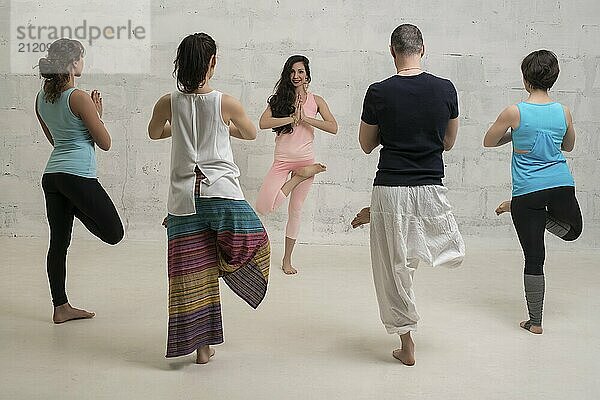 Group of women and their male trainer in sportswear doing yoga view against brick wall