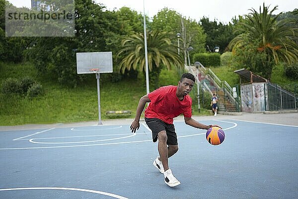 Full length photo of an african american sportive young man playing basketball outdoors