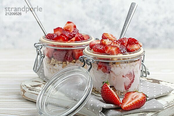 Parfait mit frischen Erdbeeren  Joghurt und knusprigem Müsli in durchsichtigen Einmachgläsern auf weißem  rustikalem Holzhintergrund aus der Vogelperspektive  gesundes Frühstück oder leichtes Sommerfruchtdessert  Foodfotografie  food photography  food photography