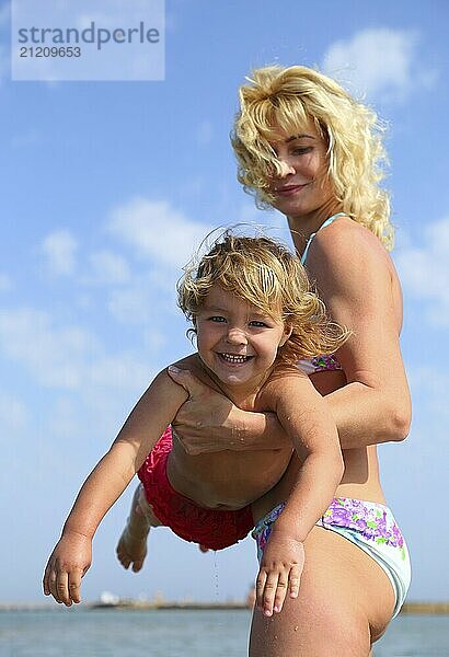 Mother holding happy baby in her arms on the beach