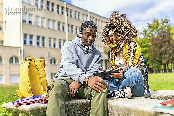 Young male and female diverse university student using tablet while sitting on steps outdoors at the university campus