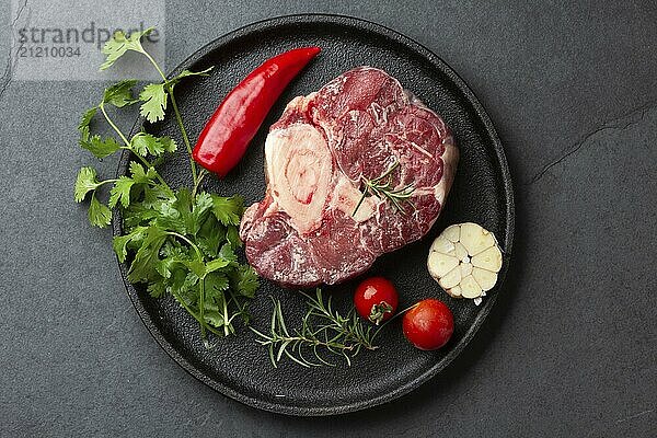 Lebensmittel  Rohes frisches Ossobuco mit Kräutern  Knoblauch und Chilipfeffer auf schwarzem Teller. Dunkler Hintergrund