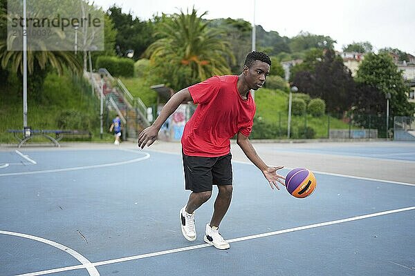 Full length african young man playing on the basketball court and dribbling a ball