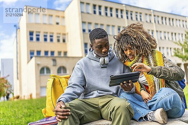 Group of diverse students looking at digital tablet sitting outdoors