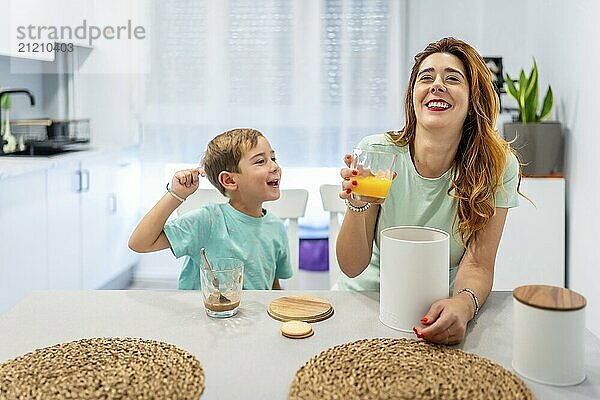 Mother and boy laughing while eating breakfast before going to school at home