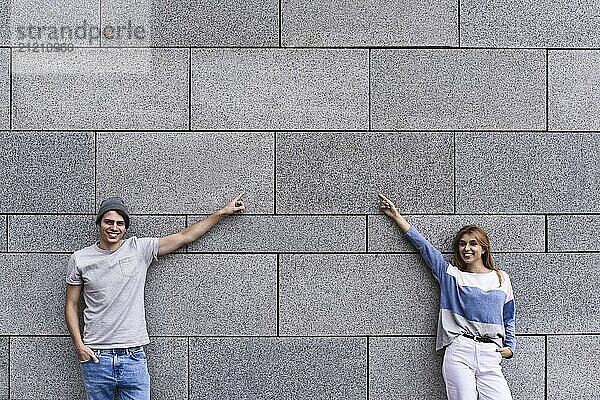 Cheerful couple at the street  show a big sale  or nice offer. Advertise concept. People  travel and tourism  on city street and couple show with their fingers something over gray wall background