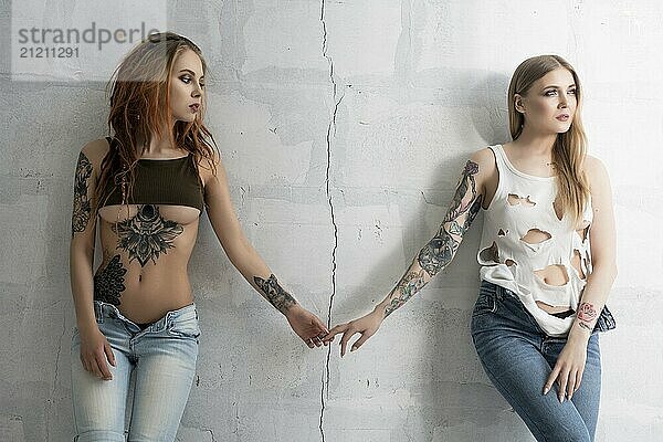 Sexy tattooed girls holding hands cropped view against cracked brick wall