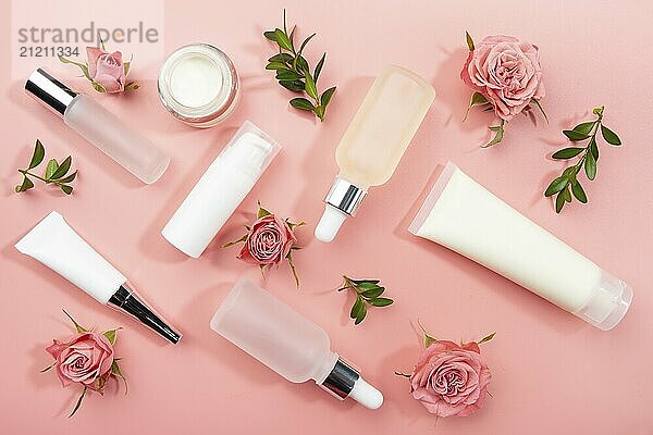 Flat lay cosmetic bottles and containers with roses and green leaves on pink background