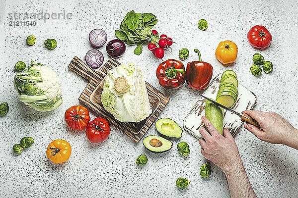 Frisches Gemüse und männliche Hände schneiden Zucchini mit Messer auf hölzernen Schneidebrett auf weißen Küchentisch Draufsicht. Kochen vegetarische Mahlzeit aus gesunden Zutaten  Diät Lebensmittel und Ernährung Konzept  Lebensmittel Fotografie  food photography  food photography