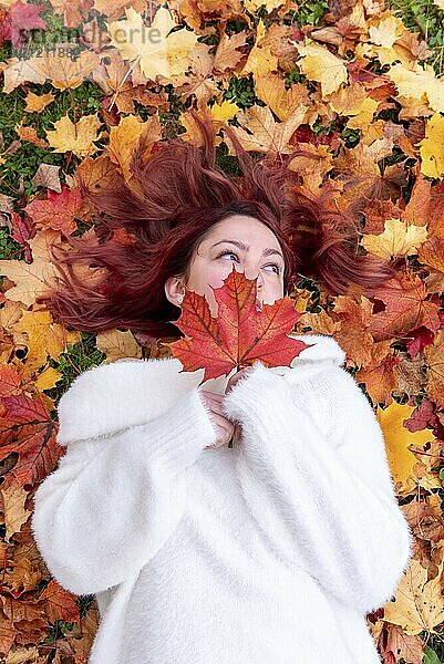 Above view with a beautiful young woman lying on the ground surrounded by autumn leaves