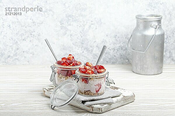 Parfait mit Erdbeeren  Joghurt und Müsli in durchsichtigen Einweckgläsern auf weißem  rustikalem Holzhintergrund aus Schrägansicht und Aluminium Milchkanne  gesundes Frühstück oder Sommerdessert  Copy Space  Foodfotografie  food photography  food photography