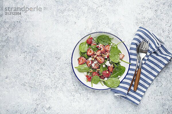 Leichter gesunder Sommersalat mit frischen Erdbeeren  Spinat  Frischkäse und Walnüssen auf weißem Keramikteller  weißer rustikaler Steinhintergrund von oben  Platz für Text  Foodfotografie  food photography  food photography