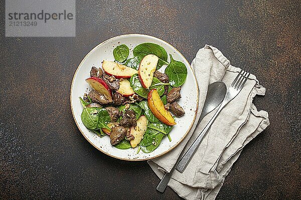 Gesunder Salat mit eisenreichen Zutaten Hühnerleber  Äpfel  frischer Spinat und Walnüsse auf weißem Keramikteller  dunkelbrauner rustikaler Steinhintergrund von oben  Foodfotografie