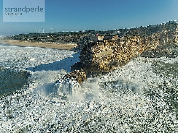 Aerial view of lighthouse on a cliff with a fortress on the coast of the Atlantic ocean with big waves at sunset in Nazare  Portugal  Europe