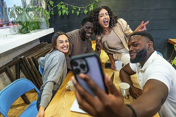 Afrikanischer Mann macht Selfie mit verschiedenen Kollegen in der Cafeteria eines Coworking Centers