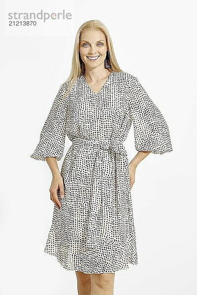 A confident woman stands indoors wearing a stylish dress adorned with a distinctive pattern