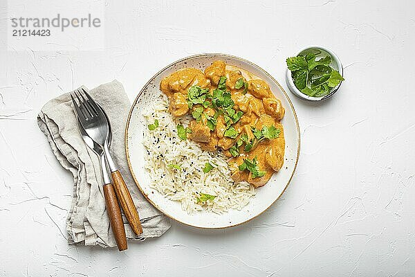 Traditional Indian dish chicken curry with basmati rice and fresh cilantro on rustic white plate on white concrete table background from above. Indian dinner meal  food photography