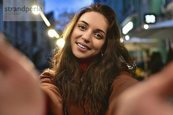 Happy elegant young woman in red coat taking selfies while walking around the city. woman hugs her boyfriend