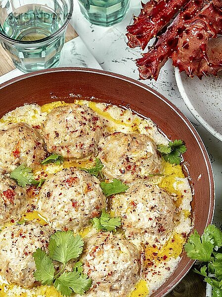 Food  Food  CRABMEATBALLS crab meatballs in white creamy sauce in red pan  whole king crab  cilantro  lemon and white wine on white background