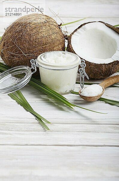 Coconut oil in airtight glass jar spoon and shell pieces on white wooden table