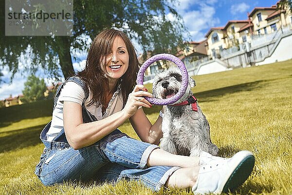 Caucasian joyful woman playing with her beloved dog in the park. The concept of love for animals. best friends. Dog breed Schnauzer