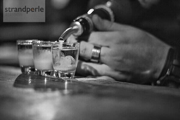 Black and white image of bartender filling shots at the counter. Selective focus