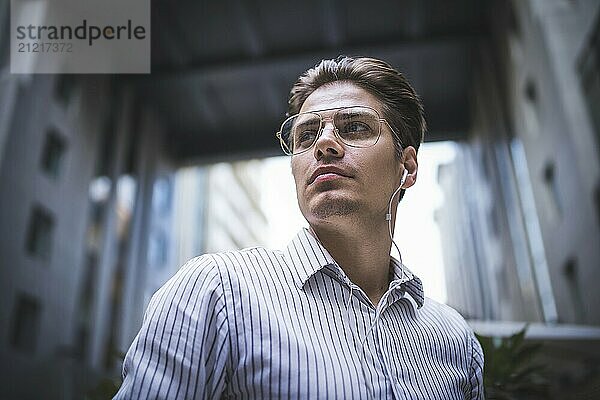 Happy handsome businessman at street with headphones looking through shoulder